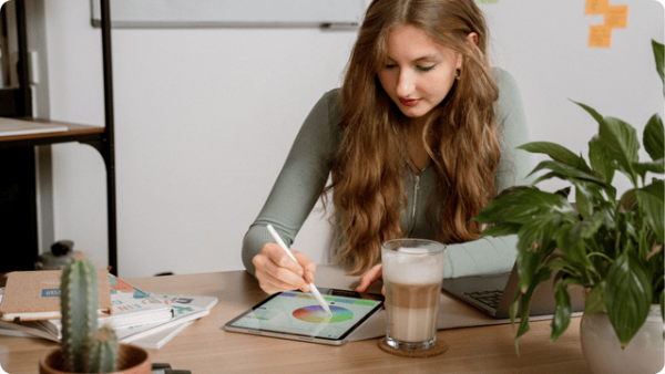 Junge Frau erstellt Farbkonzepte auf einem Tablet. Sie sitzt in einem modernen Büro.